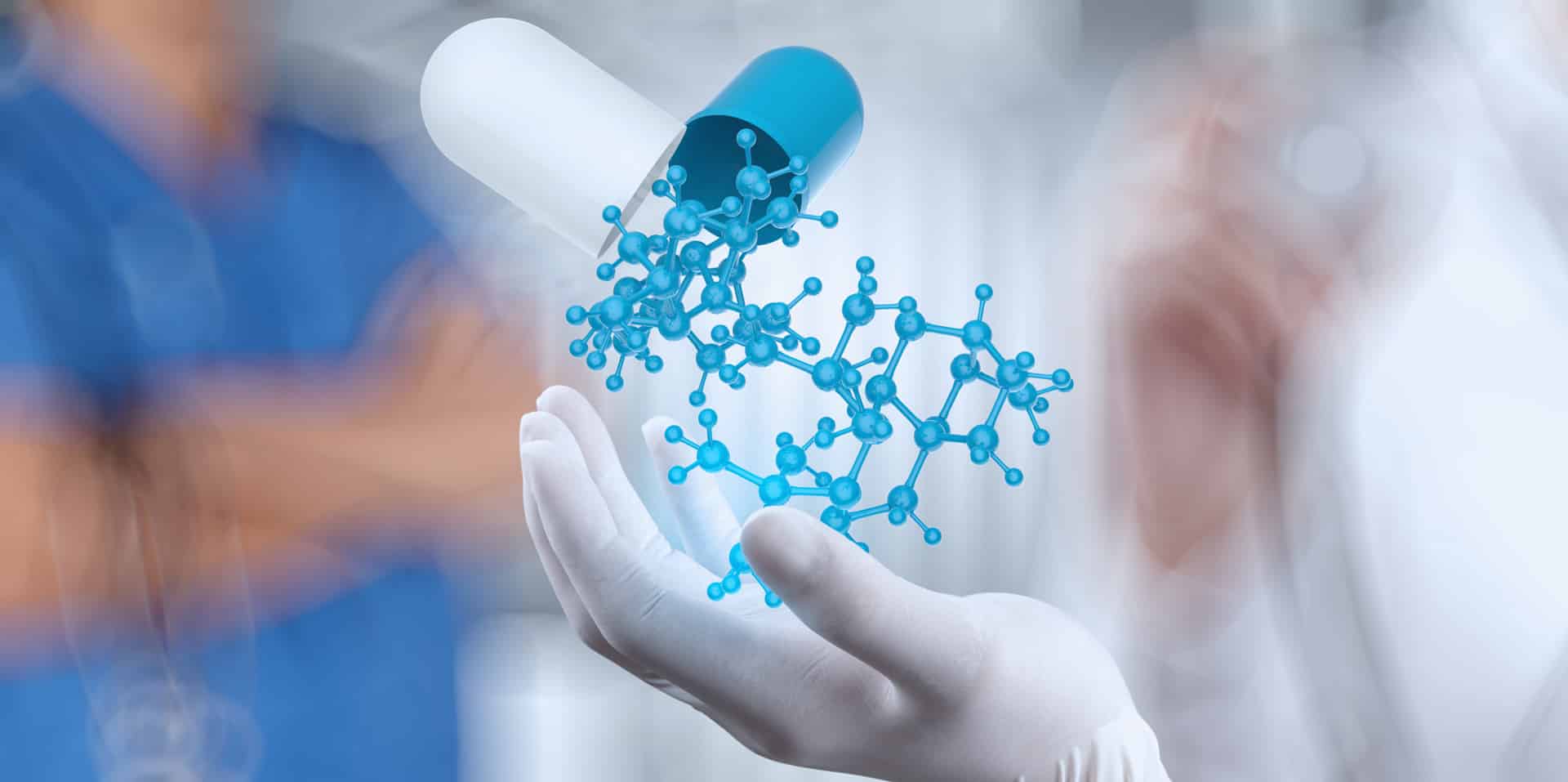 Laboratory researcher holding a pharmaceutical capsule beside a molecular model